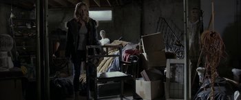 Movie still from “Clown” (2014), directed by Jon Watts – A woman standing next to a chair in a room; Wide shot, Over the shoulder angle