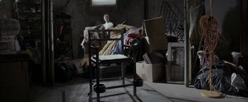 Movie still from “Clown” (2014), directed by Jon Watts – A chair and a box in a cluttered room; Wide shot, High angle