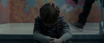 Movie still from “Clown” (2014), directed by Jon Watts – A young boy sitting on the ground with his hands folded together; Medium shot, High angle