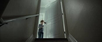 Movie still from “Clown” (2014), directed by Jon Watts – A young boy standing in front of an open door; Wide shot, Low angle