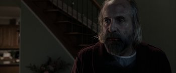 Movie still from “Clown” (2014), directed by Jon Watts – An old man with a beard and a mustache is standing in front of a staircase; Close Up shot, Over the shoulder angle