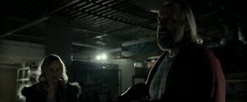 Movie still from “Clown” (2014), directed by Jon Watts – A bearded man standing in a dark room; Medium shot, Over the shoulder angle