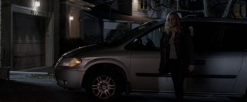 Movie still from “Clown” (2014), directed by Jon Watts – A woman standing next to a car on a street; Wide shot, High angle