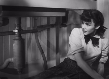 Movie still from “Cluny Brown” (1946), directed by Ernst Lubitsch – A woman sitting under a table wearing a bow tie; Medium shot, Overhead angle