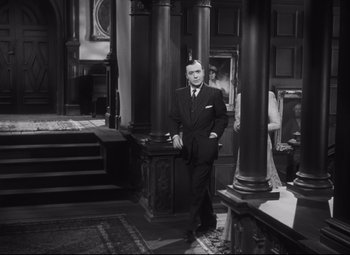 Movie still from “Cluny Brown” (1946), directed by Ernst Lubitsch – A man in a suit standing in front of pillars; Medium shot, Low angle