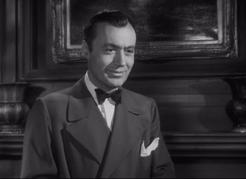 Movie still from “Cluny Brown” (1946), directed by Ernst Lubitsch – A man wearing a suit and bow tie in front of a painting; Close Up shot, Low angle