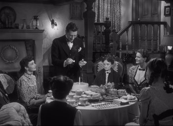 Movie still from “Cluny Brown” (1946), directed by Ernst Lubitsch – A man lighting a candle at a table with a group of people; Medium shot, High angle