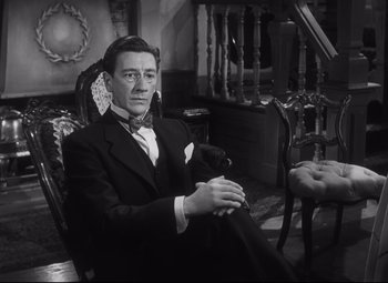 Movie still from “Cluny Brown” (1946), directed by Ernst Lubitsch – A man sitting in a chair wearing a suit and bow tie; Medium shot, High angle