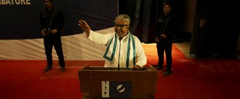 Movie still from “Cobra” (2022), directed by R. Ajay Gnanamuthu – An older man wearing a white shirt and a blue and white scarf; Medium shot, High angle