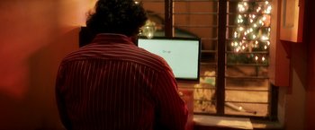 Movie still from “Cobra” (2022), directed by R. Ajay Gnanamuthu – A man sitting in front of a computer monitor; Close Up shot, Over the shoulder angle