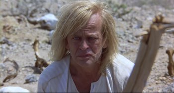 Movie still from “Cobra Verde” (1987), directed by Werner Herzog – A man with blonde hair is sitting on the ground; Close Up shot, Low angle