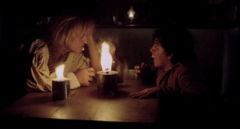 Movie still from “Cobra Verde” (1987), directed by Werner Herzog – A couple of people sitting at a table with a lit candle; Medium shot, Over the shoulder angle