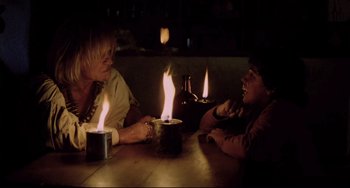 Movie still from “Cobra Verde” (1987), directed by Werner Herzog – Two people sitting at a table in front of lit candles; Medium shot, Over the shoulder angle