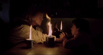Movie still from “Cobra Verde” (1987), directed by Werner Herzog – Two people sitting at a wooden table with lit candles; Medium shot, Over the shoulder angle