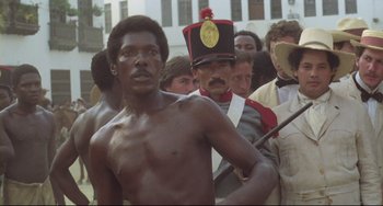 Movie still from “Cobra Verde” (1987), directed by Werner Herzog – A group of men standing next to each other in a crowd; Medium shot, High angle
