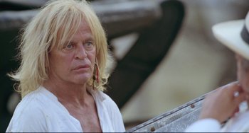 Movie still from “Cobra Verde” (1987), directed by Werner Herzog – A man with blonde hair and a white shirt is looking at the camera; Close Up shot, Low angle