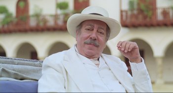Movie still from “Cobra Verde” (1987), directed by Werner Herzog – An older man wearing a white suit and a white hat; Close Up shot, Low angle