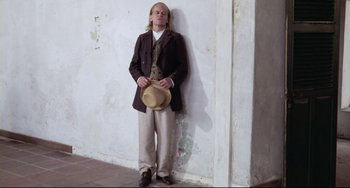 Movie still from “Cobra Verde” (1987), directed by Werner Herzog – A man leaning up against a wall with his hands in his pockets; Wide shot, Low angle