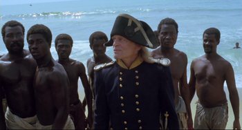 Movie still from “Cobra Verde” (1987), directed by Werner Herzog – A man in a pirate hat standing in front of a group of men; Medium shot, High angle