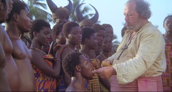 Movie still from “Cobra Verde” (1987), directed by Werner Herzog – A group of people standing around a man with horns on his head; Medium shot, High angle