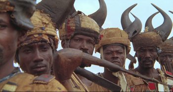 Movie still from “Cobra Verde” (1987), directed by Werner Herzog – A group of men wearing horns and holding weapons; Close Up shot, Low angle