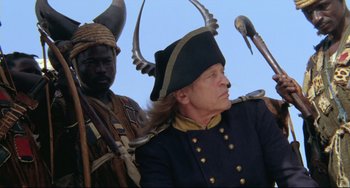 Movie still from “Cobra Verde” (1987), directed by Werner Herzog – A man in a hat and a man in a uniform; Medium shot, Low angle