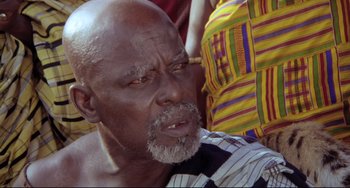 Movie still from “Cobra Verde” (1987), directed by Werner Herzog – An older man with a beard and a striped shirt; Close Up shot, High angle