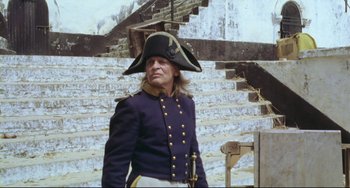 Movie still from “Cobra Verde” (1987), directed by Werner Herzog – A man in a military uniform stands in front of stairs; Medium shot, Low angle