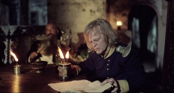 Movie still from “Cobra Verde” (1987), directed by Werner Herzog – A man sitting at a wooden table with a candle; Medium shot, Low angle