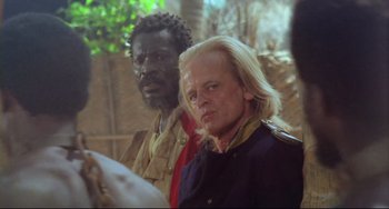 Movie still from “Cobra Verde” (1987), directed by Werner Herzog – A man in a military uniform standing next to another man in a military uniform; Close Up shot, Over the shoulder angle