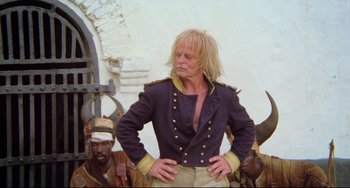 Movie still from “Cobra Verde” (1987), directed by Werner Herzog – A man standing in front of a group of men; Medium shot, Low angle