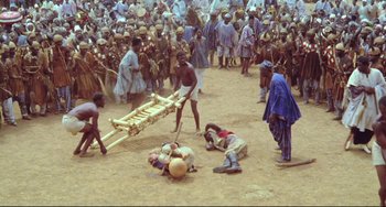 Movie still from “Cobra Verde” (1987), directed by Werner Herzog – A group of people gathered in the dirt; Wide shot, High angle