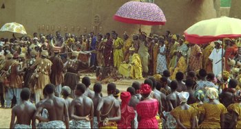 Movie still from “Cobra Verde” (1987), directed by Werner Herzog – A group of people gathered in a circle under an umbrella; Extreme Wide shot, High angle