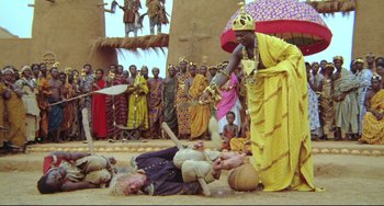 Movie still from “Cobra Verde” (1987), directed by Werner Herzog – A group of people standing around a group of men; Wide shot, High angle