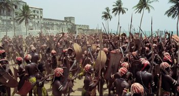 Movie still from “Cobra Verde” (1987), directed by Werner Herzog – A large group of people are gathered in a field; Extreme Wide shot, High angle