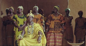 Movie still from “Cobra Verde” (1987), directed by Werner Herzog – A group of women in traditional clothing and a man in a yellow robe; Medium shot, Low angle