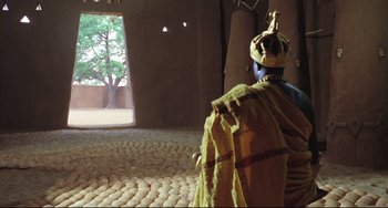 Movie still from “Cobra Verde” (1987), directed by Werner Herzog – A man in a yellow robe and a yellow turban; Wide shot, Over the shoulder angle
