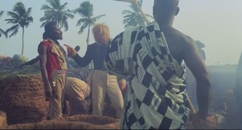 Movie still from “Cobra Verde” (1987), directed by Werner Herzog – A group of people standing next to each other on a beach; Medium shot, High angle