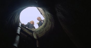 Movie still from “Cobra Verde” (1987), directed by Werner Herzog – A man and a woman standing inside of a wooden structure; Wide shot, Low angle