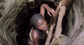 Movie still from “Cobra Verde” (1987), directed by Werner Herzog – A woman climbing up the side of a tree trunk; Medium shot, High angle