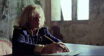 Movie still from “Cobra Verde” (1987), directed by Werner Herzog – A man sitting at a table writing on a piece of paper; Medium shot, Low angle