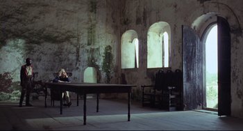 Movie still from “Cobra Verde” (1987), directed by Werner Herzog – A woman sitting at a table in an abandoned building; Extreme Wide shot, High angle