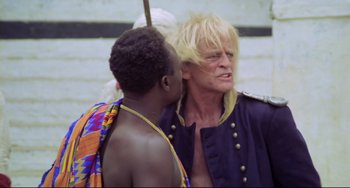 Movie still from “Cobra Verde” (1987), directed by Werner Herzog – A man with blonde hair is talking to another man; Close Up shot, Over the shoulder angle
