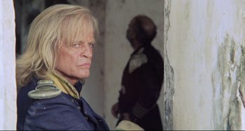 Movie still from “Cobra Verde” (1987), directed by Werner Herzog – A man with blonde long hair and a man in a uniform; Close Up shot, Low angle