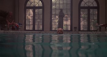Movie still from “Cocoon” (1985), directed by Ron Howard – A man swimming in a large pool of water in front of a statue; Wide shot, Low angle
