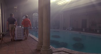 Movie still from “Cocoon” (1985), directed by Ron Howard – Two people walking by a pool in a building; Wide shot, High angle