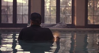 Movie still from “Cocoon” (1985), directed by Ron Howard – A man sitting in a pool in front of a window; Medium shot, Over the shoulder angle