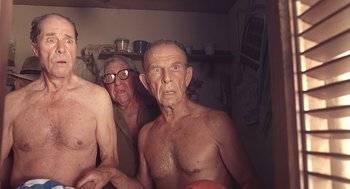 Movie still from “Cocoon” (1985), directed by Ron Howard – Two shirtless men in a room with glasses on; Medium shot, Overhead angle