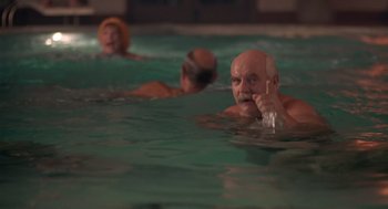 Movie still from “Cocoon” (1985), directed by Ron Howard – A group of people swimming in a swimming pool at night; Medium shot, Over the shoulder angle