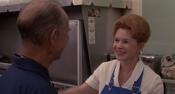 Movie still from “Cocoon” (1985), directed by Ron Howard – An older man and a woman are shaking hands in a kitchen; Medium shot, Over the shoulder angle